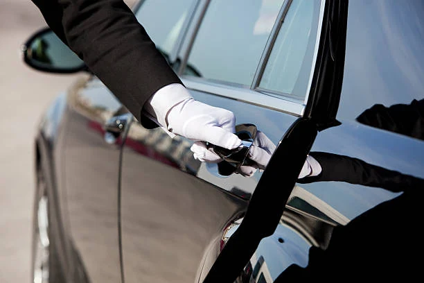 Chauffeur in formal attire opening the rear door of a black luxury sedan