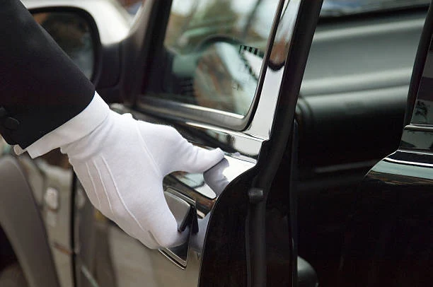 Chauffeur in white gloves opening the door of a polished black executive car