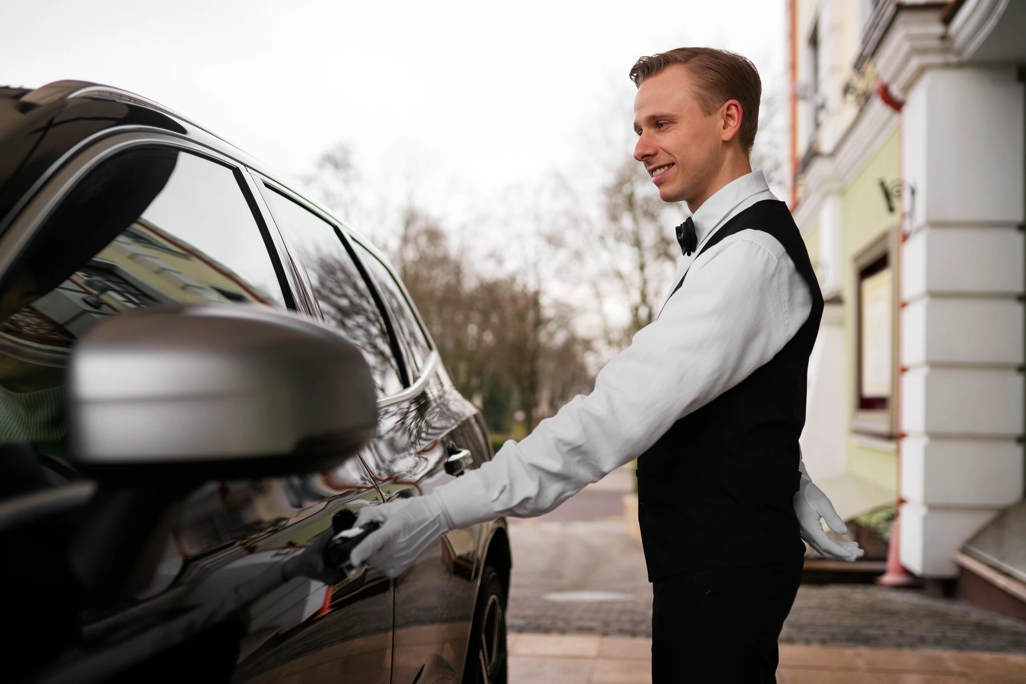 Professional valet in formal dress opening the door of a luxury vehicle