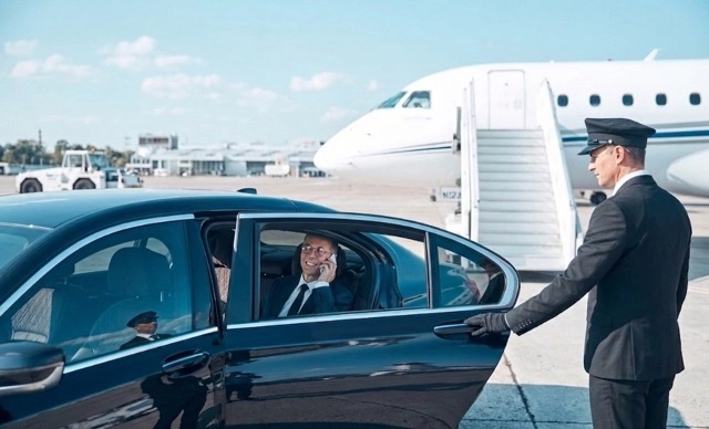 Business traveller with luggage beside a luxury saloon on the airport apron at sunset