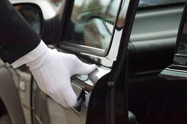 Chauffeur in white gloves welcoming a client to a black executive saloon for concierge-led travel
