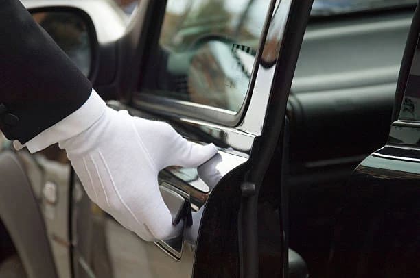 Chauffeur in white gloves welcoming a client to a black executive saloon for concierge-led travel
